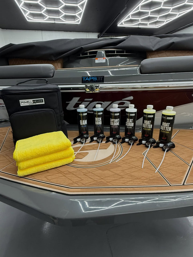 Dock Father organizer bag, six cleaner bottles and three yellow towels arranged on a boat swim platform inside a detailing shop.